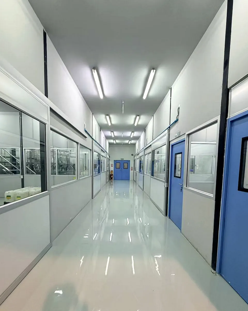 Factory corridor with production rooms visible through windows at Sawatdee Group’s Samut Prakan facility.
